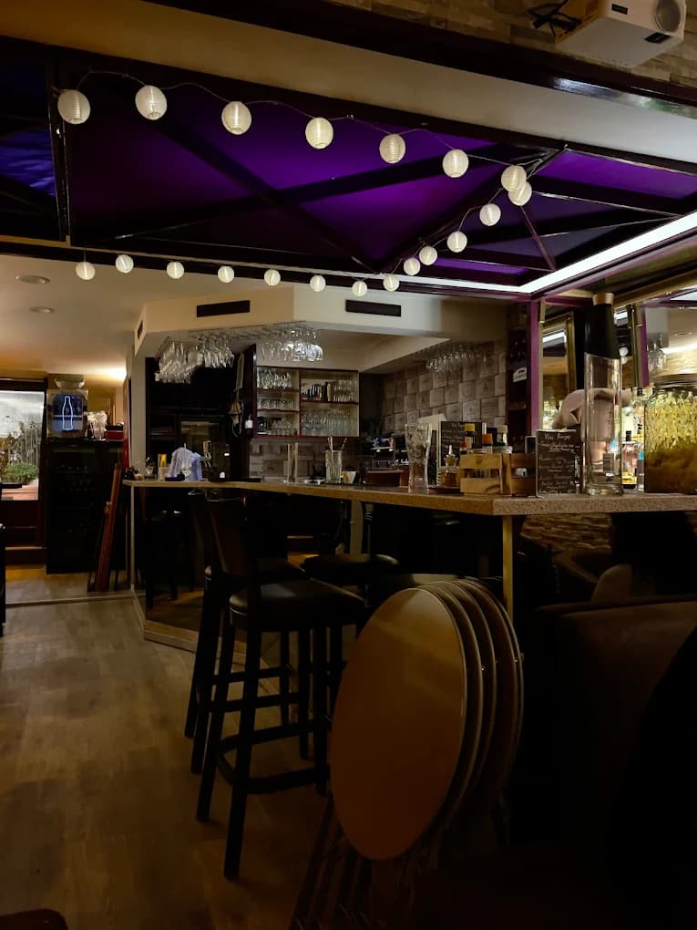 Intérieur du Studio Café : comptoir en bois, bouteilles et plafond drapé de violet éclairé de lampions